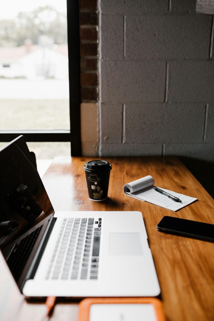 "Workspace setup with laptop, coffee cup, notepad, and smartphone near a window – a productive environment representing the best digital marketing agency in action."